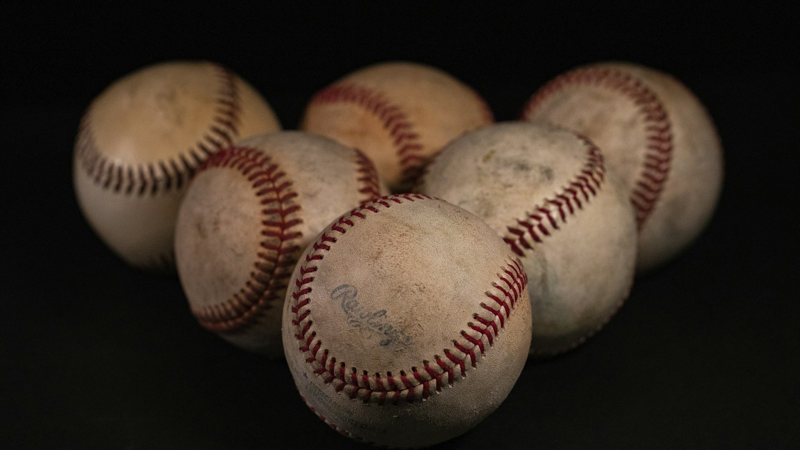 Varias pelotas de béisbol usadas sobre una superficie oscura; fotografía de archivo ilustrativa